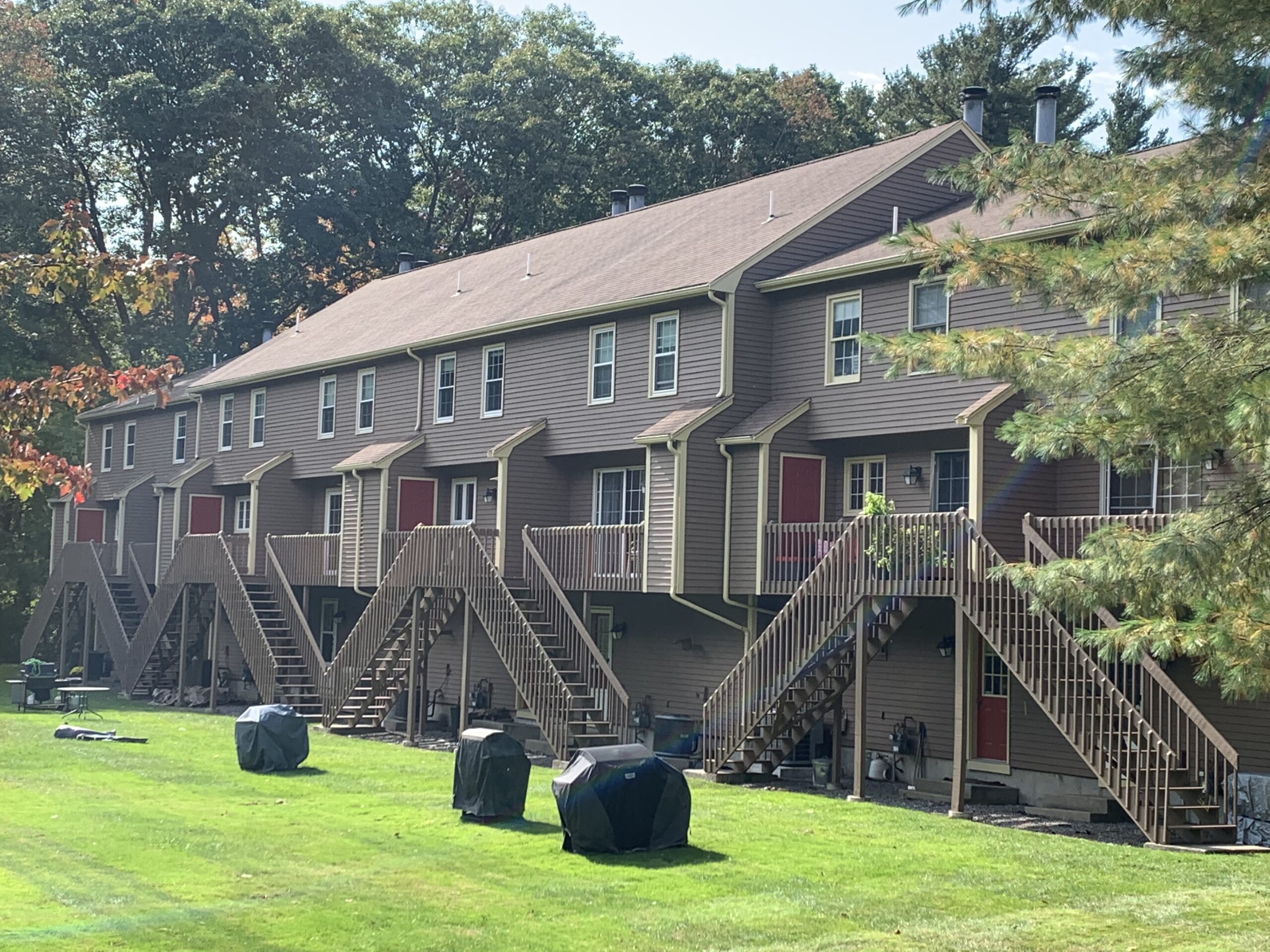 Row of townhouses with elevated wooden decks overlooking a grassy communal area with trash bins.