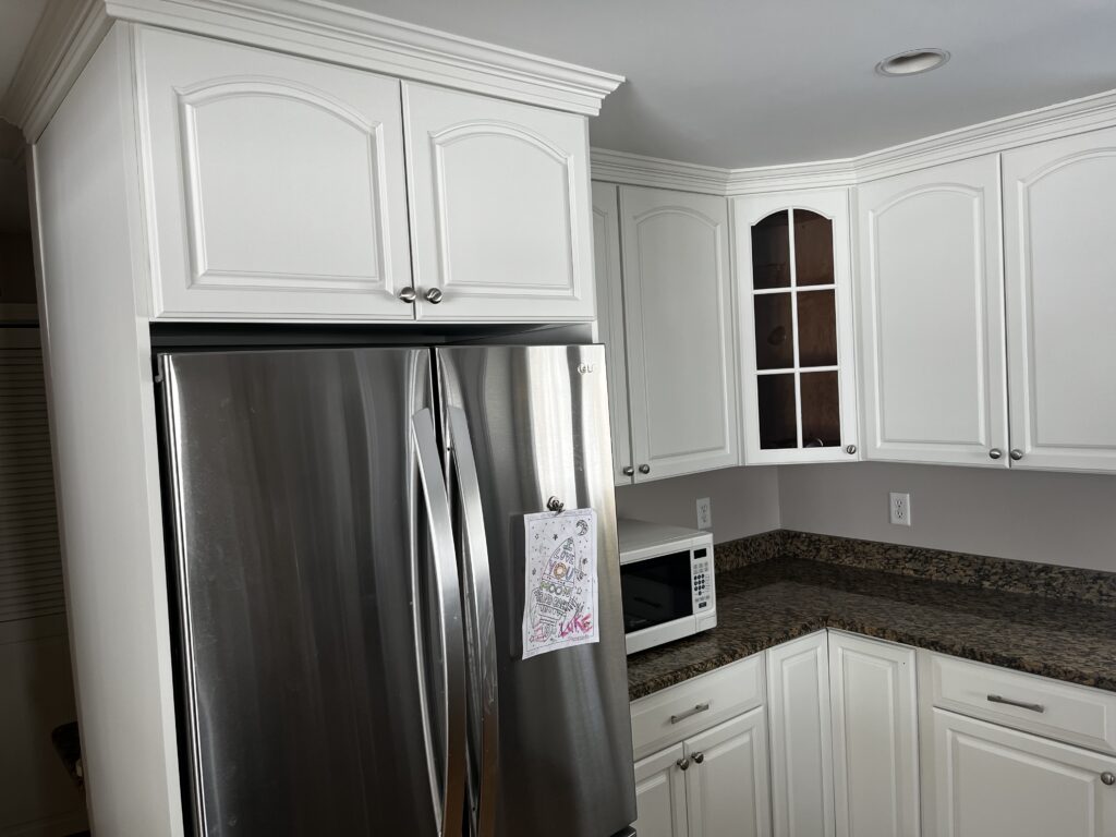 Modern kitchen featuring stainless steel refrigerator, white cabinetry, and a granite countertop, showcasing a clean and organized space.
